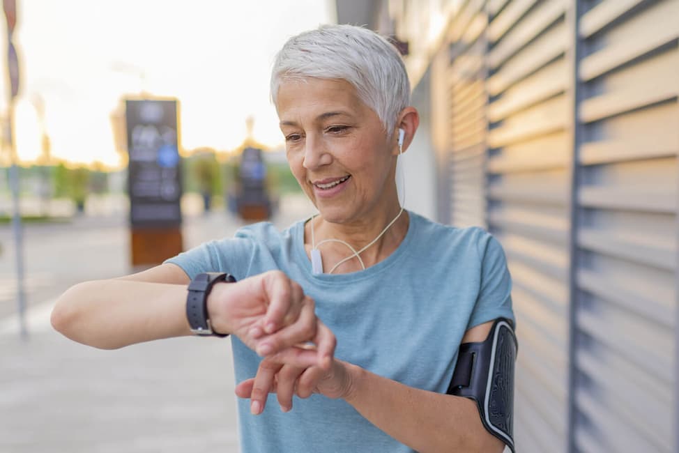 older woman outside with earbuds checking her watch